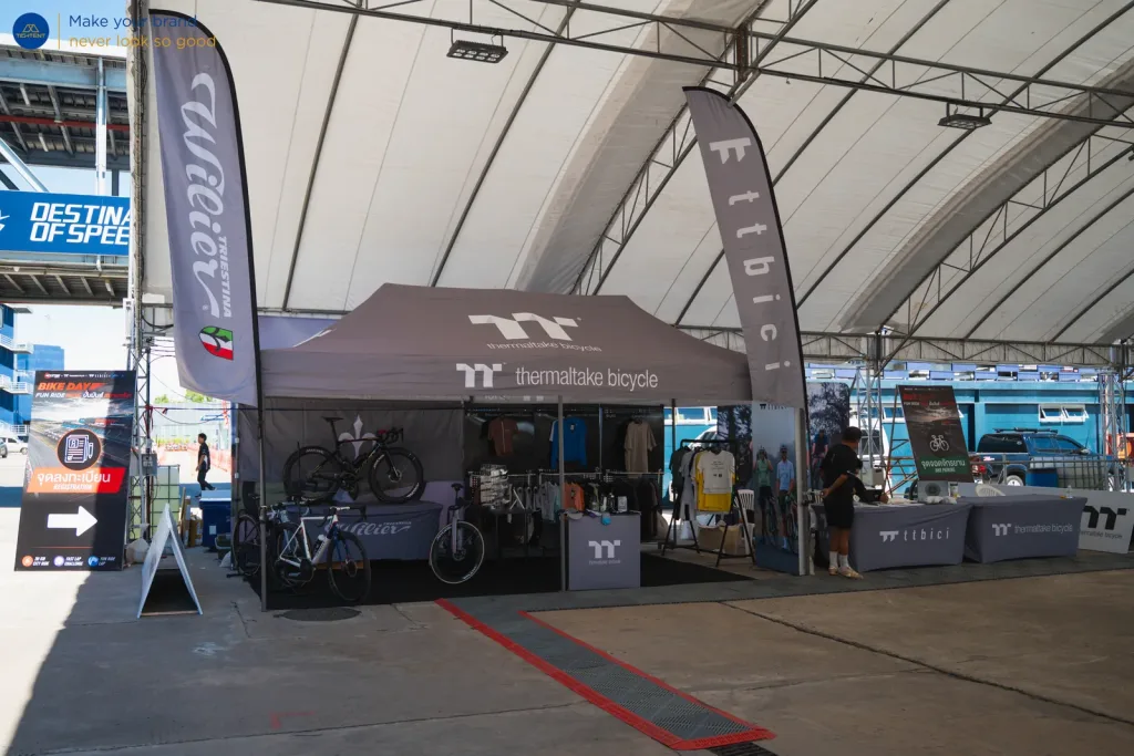 เต็นท์พับ Thermaltake Bicycle ในโรงจอด พร้อมธงปีกนกและผ้าคลุมโต๊ะพิมพ์โลโก้