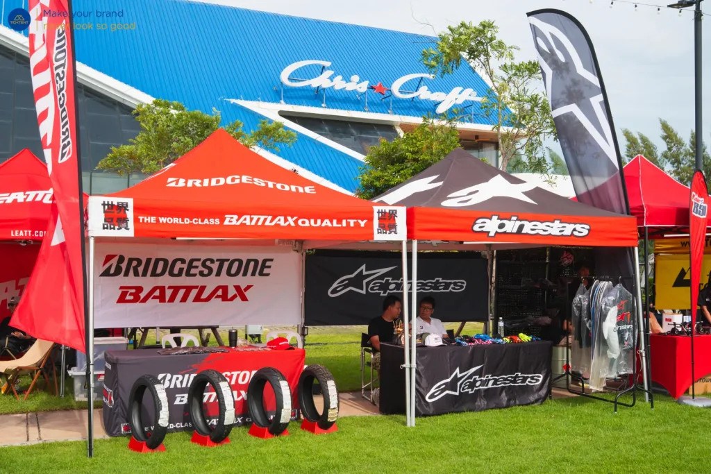 เต็นท์พับ Bridgestone Battlax และ Alpinestars พร้อมผ้าคลุมโต๊ะพิมพ์โลโก้และธงปีกนก