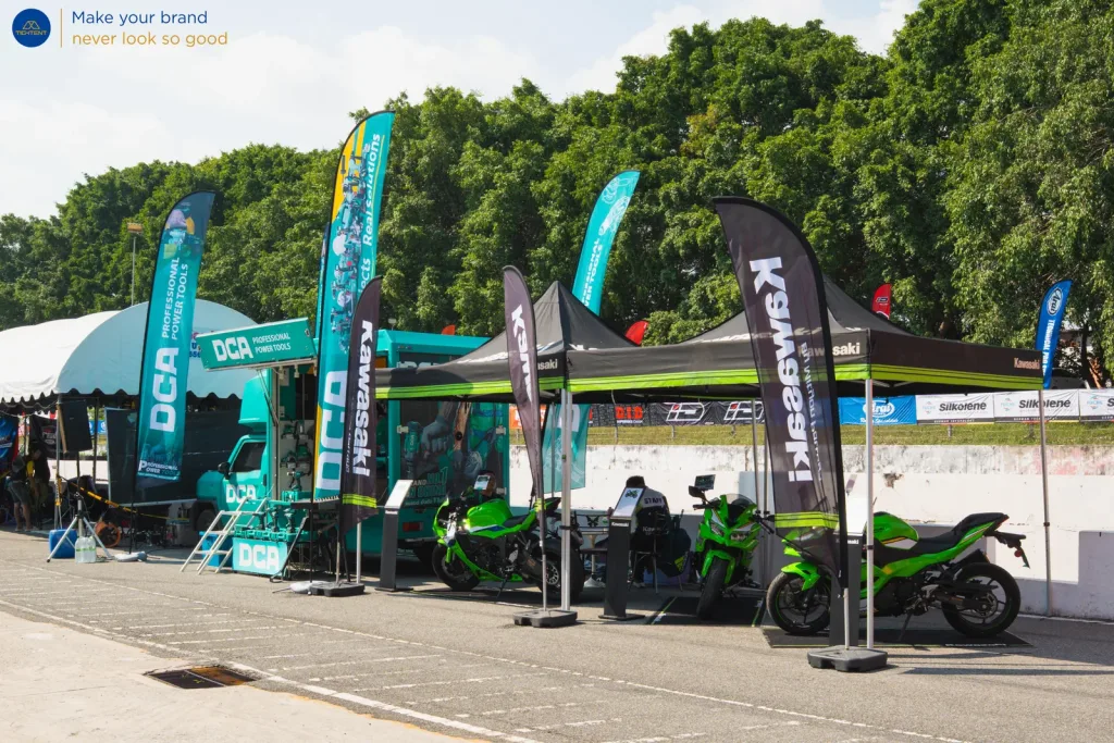 ธงปีกนก Kawasaki และ DCA หน้าเต็นท์พับและรถที่จัดแสดง