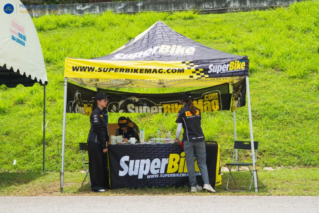 ทีมงานใต้เต็นท์พับ SuperBike ที่โต๊ะหุ้มผ้าพิมพ์โลโก้